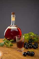 Jaboticaba, bottle and glass of homemade Brazilian jaboticaba liqueur on wood with leaves and branches and also jaboticaba making up the scene, light background, selective focus.
