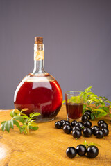 Jaboticaba, bottle and glass of homemade Brazilian jaboticaba liqueur on wood with leaves and branches and also jaboticaba making up the scene, light background, selective focus.