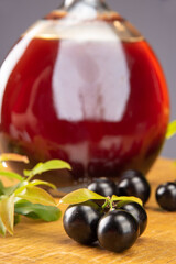 Jaboticaba, bottle and glass of homemade Brazilian jaboticaba liqueur on wood with leaves and branches and also jaboticaba making up the scene, light background, selective focus.