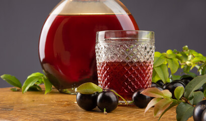 Jaboticaba, bottle and glass of homemade Brazilian jaboticaba liqueur on wood with leaves and branches and also jaboticaba making up the scene, light background, selective focus.