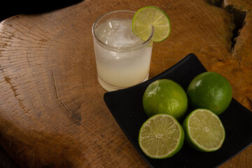 Brazilian drink caipirinha, glass of caipirinha and lemons on rustic wood light background, selective focus.