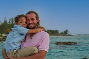 Fototapeta premium A mixed race father and son. The modern dad has dreadlocks and the pair are enjoying an awesome day at the beach