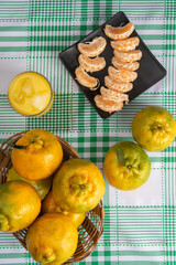 Orange ponkan, orange ponkan slices on a black plate, plus some oranges and a glass of juice on a checkered tablecloth on a light background, top view.