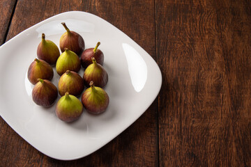 Purple figs, purple figs on a white plate on rustic wood, black background, selective focus.