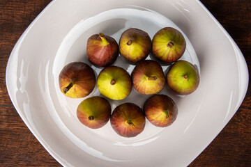 Purple figs, purple figs on a white plate on rustic wood, black background, top view.
