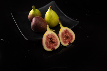 Purple figs, purple figs open on a black plate on dark reflective surface, black background,...