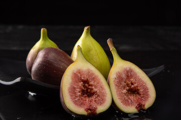 Purple figs, purple figs open on a black plate on dark reflective surface, black background,...