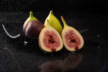 Purple figs, open purple figs being sprayed with water, black background, selective focus.