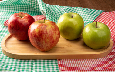 Green and red apples positioned on wood on checkered tablecloths, black background, selective focus.