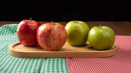Green and red apples positioned on wood on checkered tablecloths, black background, selective focus.