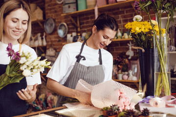 Woman florist together with assistant collect bouquets in flower shop.