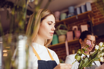 Woman florist together with assistant collect bouquets in flower shop.