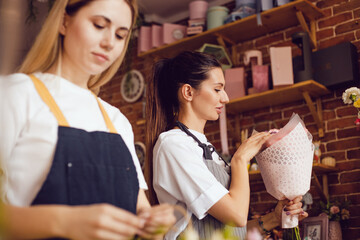 Woman florist together with assistant collect bouquets in flower shop.