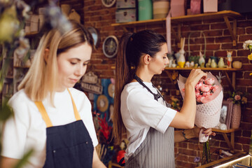 Woman florist together with assistant collect bouquets in flower shop.