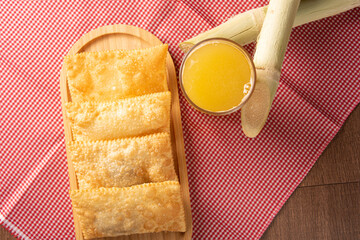 Brazilian fried pastries, a glass of sugarcane juice and canes positioned on a checkered...