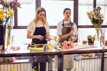 Florist girls collect bouquets of flowers at their desk in a flower shop.