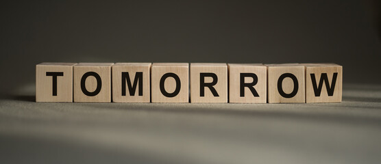 A wooden blocks with the word TOMORROW written on it on a gray background.