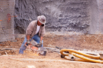 Worker using concrete saw on the ground at construction site, with sparks flying from the blade