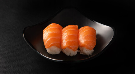 Sushi, beautiful arrangement of sushi made on black plate on dark surface, black background, selective focus.