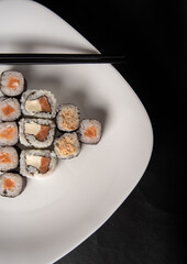 Sushi, beautiful arrangement of sushi made on a white plate on dark surface, black background, Top view.