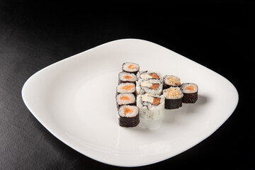 Sushi, beautiful arrangement of sushi made on a white plate on dark surface, black background, selective focus.