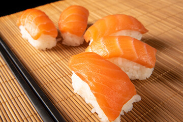 Sushi, beautiful sushi arrangement covered with hashi on a bamboo mat, on dark surface, black background, selective focus.