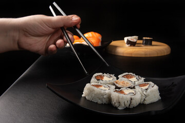 Sushi, hands picking sushi using hashi, black background, selective focus.