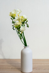 Portrait white picture frame mockup on wooden table. Modern ceramic vase with yelow freesia flowers . White wall background. Scandinavian interior. 