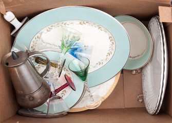 discarded fine china, liqueur stemware, and an old espresso coffee maker in a plain brown box