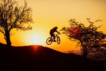 silhouette of cyclist on sunset jumping 