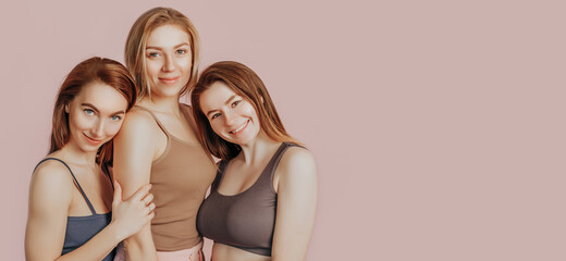 Three girls in comfortable home clothes together on a pink background. Women smile and have fun....