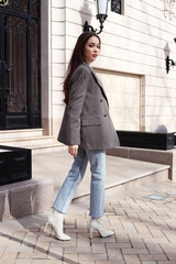 Style on the streets of the city. Young caucasian woman in a man's oversized jacket and white ankle boots with heels. Walk on a sunny, fine day off. Women trendy style
