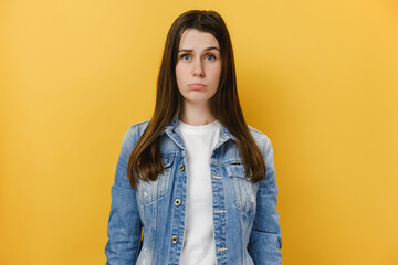 Upset young woman 20s purses lower lip, feels insulted and dissatisfied, looks sadly at camera,...