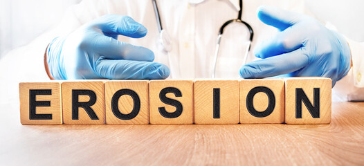 A young male doctor in blue medical gloves holds cubes with the inscription EROSION. Health and medicine concept.