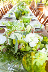 Long wood table and chairs in vineyard set for party with flowers, glassware, plates and silverware 