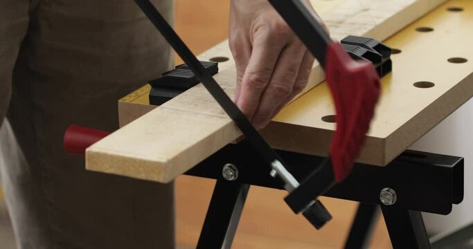 Man making starting cuts on wood plank fixed in workbench using hand saw, close-up
