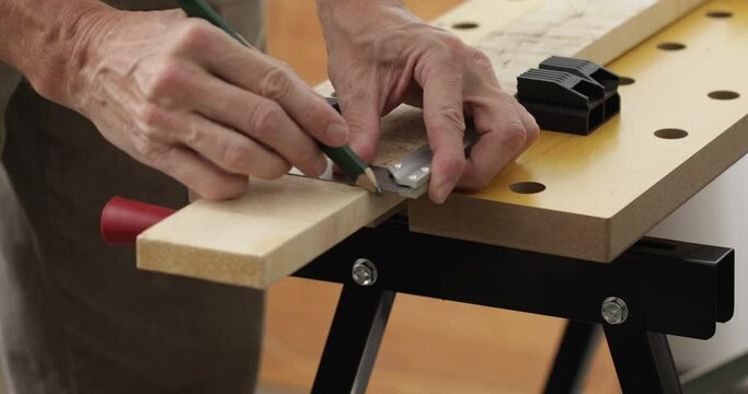 DIY woodworking, man drawing cutting lines at wood plank using square ruler and pencil, close up