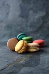 Colorful assorted french macaroon cakes on dark stone background. Side view