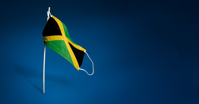 Jamaica mask on dark blue background. Waving flag of Jamaica painted on medical mask on pole. Concept of The banner of the fight against the epidemic coronavirus COVID-19. Copy space