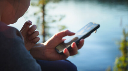 Close up. Mother using her mobile phone apps browsing chatting playing web surfing network with little daughter opposite the lake during sunset on spring camping vacation. Concept of modern technology