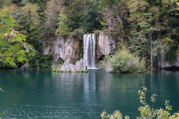 Fototapeta na wymiar Waterfall with powerful streams against the background of a lake with blue water and a mountain slope with trees on an autumn day, Plitvice Lakes National Park