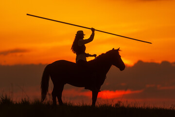 Fototapeta na wymiar Spanish motif of a horsewoman with a spear, silhouette against the setting sun