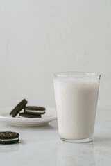 Glass of milk accompanied by some chocolate cookies filled with white cream on a white background