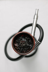 Hookah on a white plate with a red silicone bowl top view, burnt fruit tobacco after smoking. Close-up.