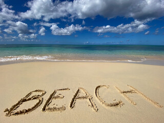 BEACH inscription on the sand with sea waves and sky. Concept of vacation and holiday