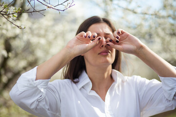Woman suffering from strong eye pain against spring trees