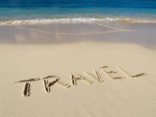 TRAVEL inscription on the sand with sea waves and sky. Concept of vacation and adventure 