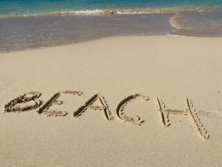 BEACH inscription on the sand with sea waves and sky. Concept of vacation and holiday