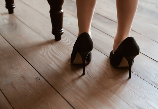 Little girl stay back in big adult mother black high heels shoes near chair at wooden floor, imitation dressing up game