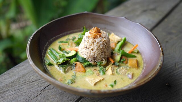 Serving a plate of healthy organic vegan green curry to the black wooden table